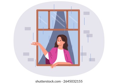 First autumn rain brings joy to woman looking out of apartment window and catching drops with smile. Happy girl enjoying view of street during rain, standing with blanket on shoulders in cozy home