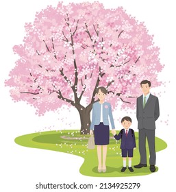 A first grade boy and his parents stand side by side in front of a cherry tree
