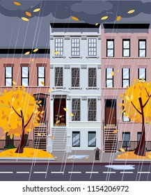 Flat cartoon vector illustration of autumn rainy city street. Three-four-story uneven houses, foliage flies. Street cityscape. Evening city landscape with autumn trees in the foreground, puddles