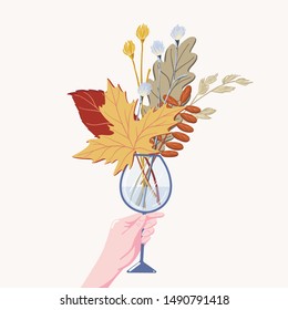 Flat cartoon vector illustration of human hand holding bouquet of fall, autumn leaves, herbs, and branches in wine glass isolated on white background. Female hand holding wine glass with fall leaves