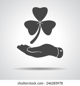 flat hand presenting  Clover with three leaves sign icon. on a grey background. Saint Patrick symbol