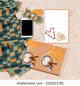 Flat lay cup of chocolate with cinnamon, marshmallow snowman and dries orange slices on wooden tray, Mobile phone, notebook, candy cane and pine branch with cones, Hot  drink for autumn or Winter 