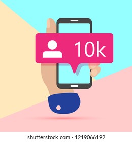 flat lay modern minimal hand holding mobile phone with new pink ten like followers social media icon on screen with shadow on pastel colored blue and pink background. 