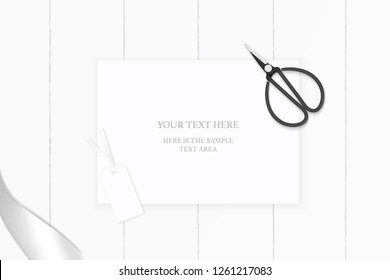 Flat lay top view elegant white composition paper silver ribbon tag and vintage metal scissors on wooden background.