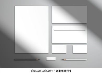 Flat layout with branding kit. White sheet of paper, two envelopes, two business cards, pencils and an eraser. Realistic template for design with shadow from the window