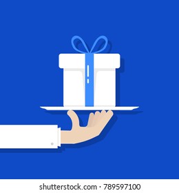 flat style hand holding white gift box on plate. cartoon graphic logo design element isolated on blue background. concept of surprise giftbox or gratitude for people and father or mother day holiday