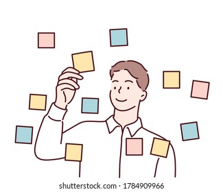 Focused young male employee writes ideas on sticky note on glass wall in office. Hand drawn style vector design illustrations.