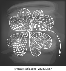 Four leaf, decorative clover filled with hand- drawn floral and geometrical patterns on chalkboard background. St. Patrick's day card.