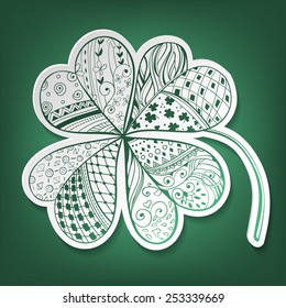 Four leaf, decorative white paper clover filled with hand- drawn floral and geometrical patterns on gradient green background. St. Patrick's day card