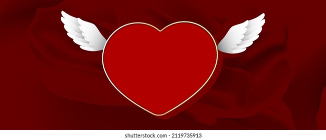 Frame in the form of a heart in a gold frame with wings on a background of red silk.