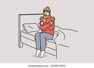 Freezing man is shaking sitting on bed and feeling chills and cold, dressed in hat and scarf. Freezing guy suffers due to lack of central heating system and poor immunity, located in bedroom