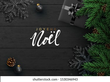 French text Joyeux Noel. Christmas background. Dark Wood plank texture, black snowflakes, realistic pine cone, decorative bauble, gift boxes. Xmas decoration objects. pine branches. Flat lay, top view