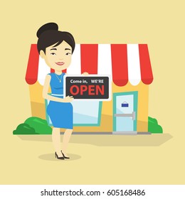 Friendly female shop owner holding open signboard. Cheerful female shop owner standing in front of small store. Woman inviting to come in her shop. Vector flat design illustration. Square layout.