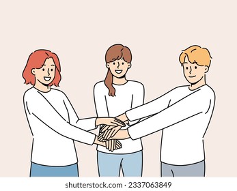 Friendly team of people holding hands demonstrate cohesion and unity, wanting to achieve goals together. Team of young guy and two girls carrying out volunteer or charitable activities