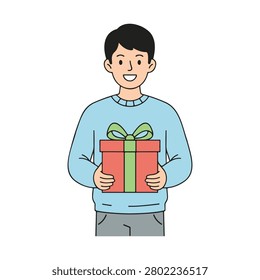 A friendly young man with dark hair wearing a light blue sweater, smiling and holding a red gift box with a bright green ribbon, isolated on white.