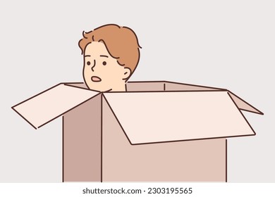 Frightened man hides in carton box and looks out to inspect area around. Frightened young guy with embarrassment hiding in cardboard package trying to avoid meeting offender or unpleasant person