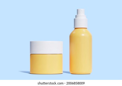 Front view of 3d orange plastic jar and spray bottle with white caps. Container elements isolated on blue background. Suitable for cosmetic kit mock up.