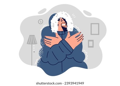 Frozen man in winter jacket is shivering from cold standing in unheated apartment and needs heater. Frozen guy suffers from high gas or electricity tariffs and needs social benefits