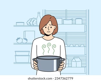 Frustrated woman housewife with pot of sour soup, feels bad smell from food spoiled due to violation of sanitary rules. Girl is standing in kitchen and holding stinking soup in bewilderment