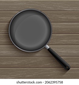 Frying black pan prepared for cooking your favorite meal is placed on a wooden table background.