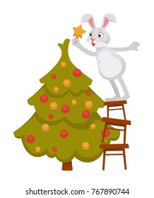 Funny bunny decorates Christmas tree and stands on ladder
