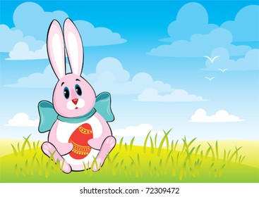 Funny cartoon rabbit and colored eggs on a green grass and blue sky