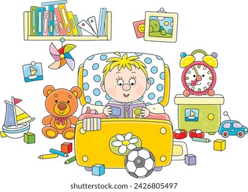Funny little boy lying in his small bed and reading an interesting book with fairy tales among funny toys in a nursery room, vector cartoon illustration isolated on a white background