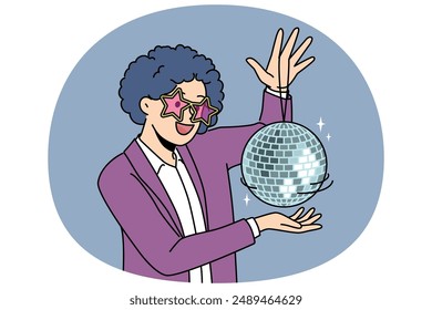 Funny man with disco ball with curly wig on head came to nightclub or dance floor to have fun and relax. Young guy enjoys atmosphere of music festival or disco party for party people