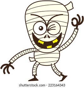 Funny mummy, with bulging eyes and broken yellow teeth, in mischievous mood while staring at you, smiling, winking and making an OK sign with its left hand