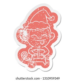 funny quirky cartoon distressed sticker of a monkey with christmas present wearing santa hat