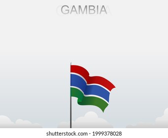 The Gambian flag flutters on a pole standing tall under a white sky