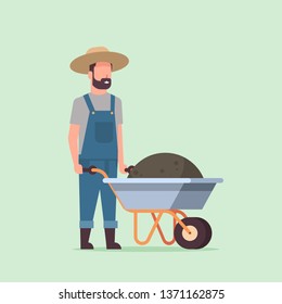 gardener man pushing wheelbarrow full of earth compost male farmer working in garden wearing overalls gardening concept full length