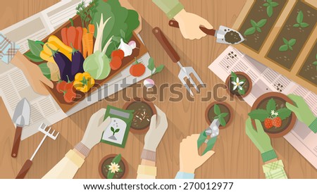 Gardeners hands working together on a wooden table top view with gardening tools, they are planting seeds and plants and carrying a vegetables crate