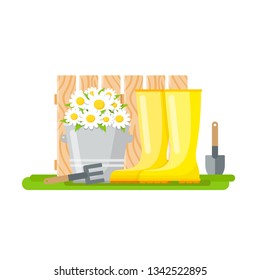 Gardening tools - rake, paddle, rubber boots and bucket with daisies on the background of a wooden fence
