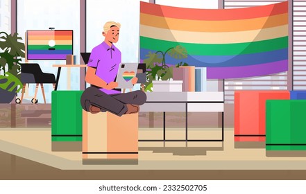 gay sitting at workplace and using tablet pc lgbt rainbow flag transgender love generation Z concept office interior