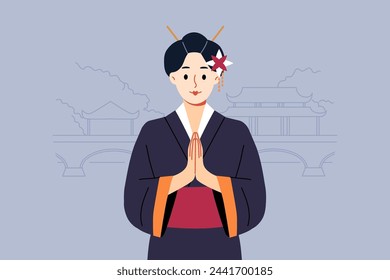 Geisha woman in traditional japanese kimono makes konishua gesture, standing near park with traditional oriental buildings. Geisha from asian country folds palms in front of chest as sign of greeting.