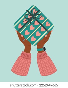 Gift box in hand. A gift wrapped in a festive paper wrapper with a tied bow, ribbon, twine, string. Christmas, Xmas, valentine's day, birthday and New Year present in wrapping paper in hands.