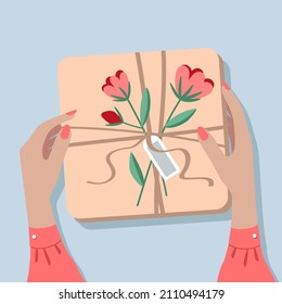 Gift box on the table, top view. The girl is holding a box in her hands. Female hands wrapping a gift in craft paper. The box is decorated with a bouquet of flowers.