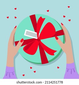Gift box with red bow on the table, top view. The girl is holding a box round in her hands. Get a gift for Valentine's Day