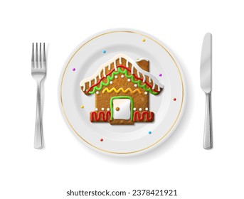 Gingerbread house is on white plate with fork and knife, top view. Dinner plate with holiday cookie inside and cutlery set on sides