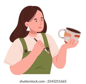 A girl in an apron paints a clay cup. Pottery.