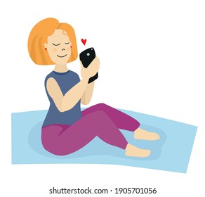 A girl with blonde hair on a yoga mat looks at her phone and receives a love message