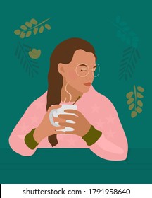 Сute girl with braid holds cup with a hot drink in her hands.There is steam from a mug with tea, cacao or coffee.Cozy autumn mood.Young woman portrait with glasses and freckles. Pink casual sweatshirt