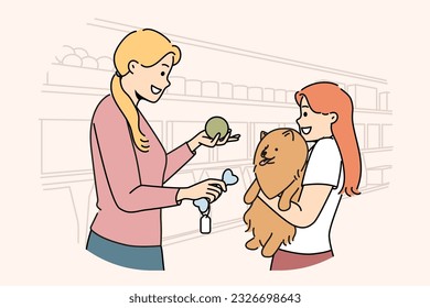 Girl with dog stands in ZOO shop near woman seller offering to buy toy bone for pet. Happy mom and little daughter choose rubber ball for their dog together after adopting puppy from shelter