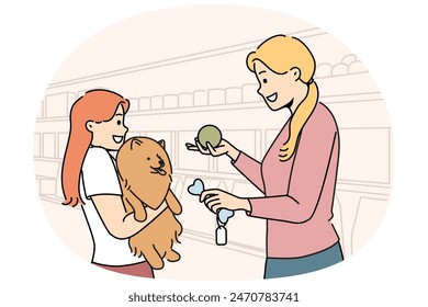 Girl with dog stands in ZOO shop near woman seller offering to buy toy bone for pet. Happy mom and little daughter choose rubber ball for their dog together after adopting puppy from shelter