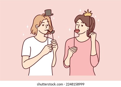 Girl friends with funny masks for photo shoot during house party or holiday carnival. Young casual women put cardboard lips and smoking pipe or crown with hat on their face. Flat vector illustration 