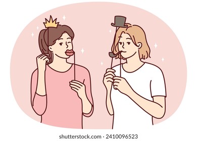 Girl friends with funny masks for photo shoot during house party or holiday carnival. Young casual women put cardboard lips and smoking pipe or crown with hat on their face. Flat vector illustration