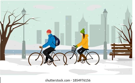 A girl and a guy ride bicycles in the park. in the background winter cityscape.