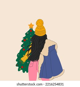 A girl in a hat and a warm jacket stands in front of a Christmas tree
