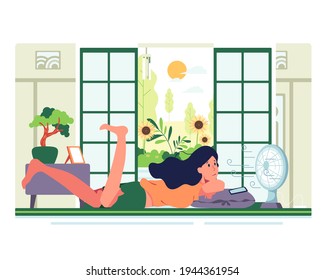 A girl with her vacation After doing all the housework, lay down and play the phone in front of the fan in the living room. In the room there are bonsai trees. There is a picture frame on the table.